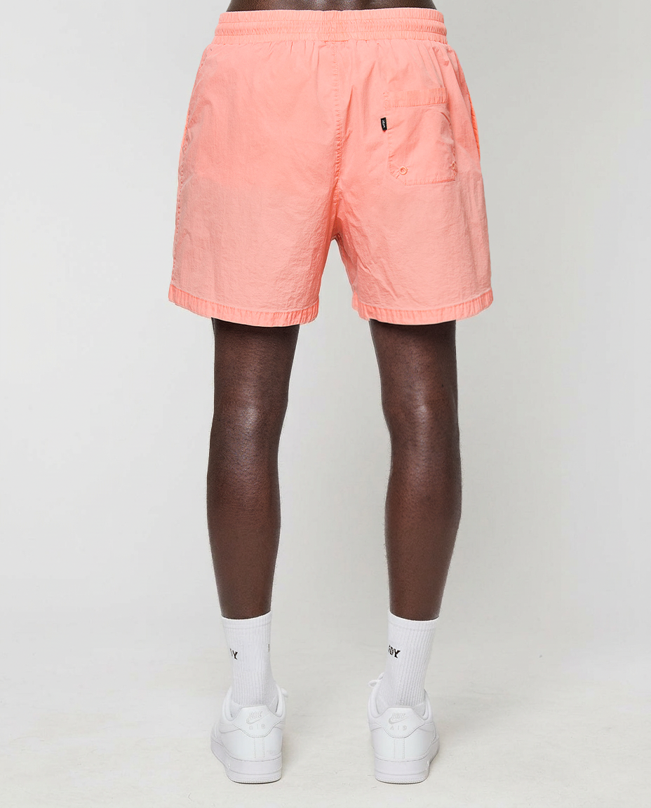 A person stands facing away, wearing LIVE FAST DIE YOUNG Live Fast Swim Shorts with an elastic waistband, white crew socks, and white sneakers against a plain light background. The shorts have a back pocket on the right side.