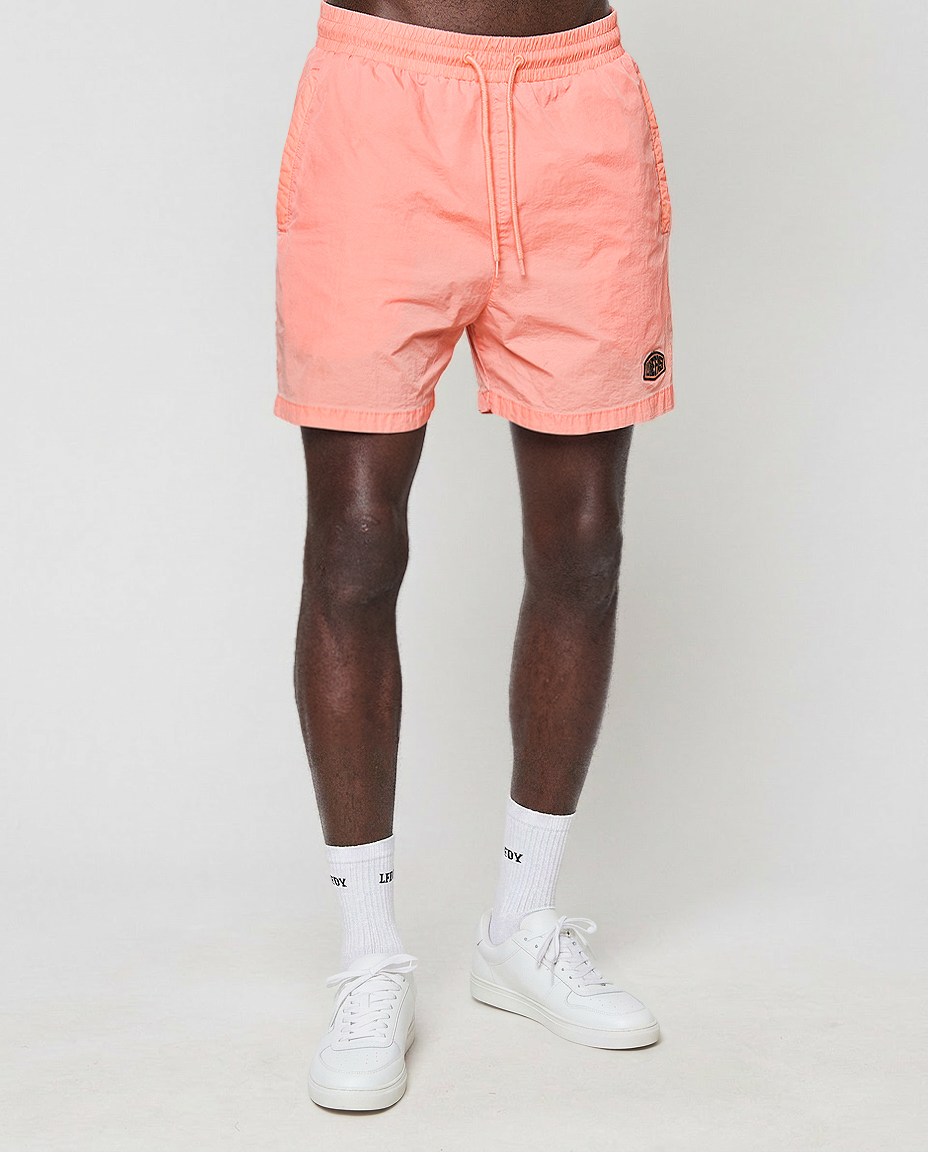 A person wearing LIVE FAST DIE YOUNG Live Fast Swim Shorts, white crew socks, and white sneakers stands against a plain light background. The photo is cropped above the waist, showing only their legs.