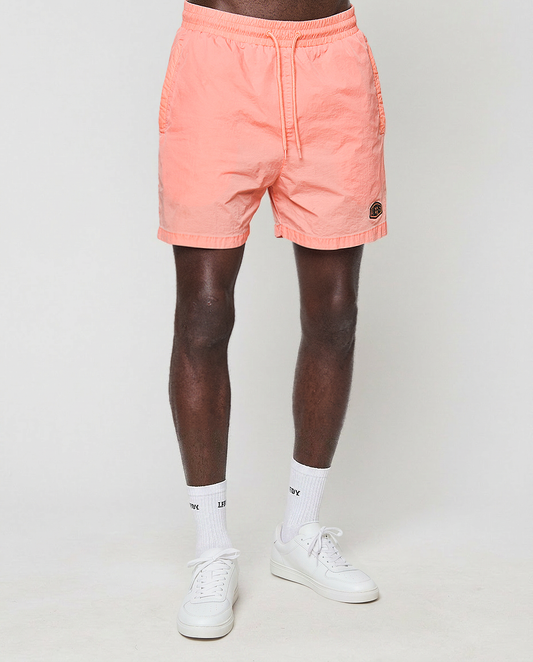 A person wearing LIVE FAST DIE YOUNG Live Fast Swim Shorts, white crew socks, and white sneakers stands against a plain light background. The photo is cropped above the waist, showing only their legs.