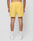 A person faces away from the camera, wearing LIVE FAST DIE YOUNG’s Live Fast Swim Shorts in yellow with an elastic waistband and tinted yellow wash, paired with white socks and sneakers against a plain light background.