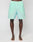 A person stands barefoot on a white surface, wearing mint green LIVE FAST DIE YOUNG Beach Shorts. The image is cropped from the waist to the feet.