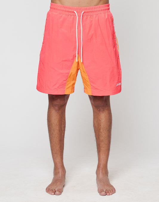 A barefoot person models LIVE FAST DIE YOUNG Beach Shorts in coral and orange colorblock with Breiter Elastikbund and white drawstrings, photographed from the waist down against a plain light background.