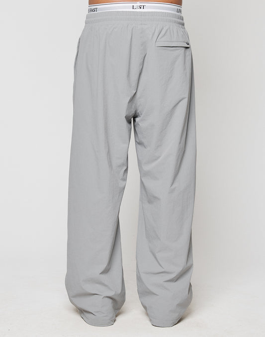 A rear view of a person wearing LIVE FAST DIE YOUNG LFDY Ripstop Trackpants in light gray, featuring an elastic waistband, single back pocket, and wide fit silhouette against a plain white background.