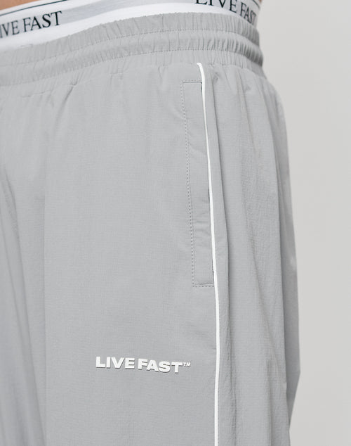 Close-up of a person wearing LIVE FAST DIE YOUNG LFDY Ripstop Trackpants in light gray with white piping. The waistband of matching underwear featuring the LIVE FAST text is visible above the trackpants.