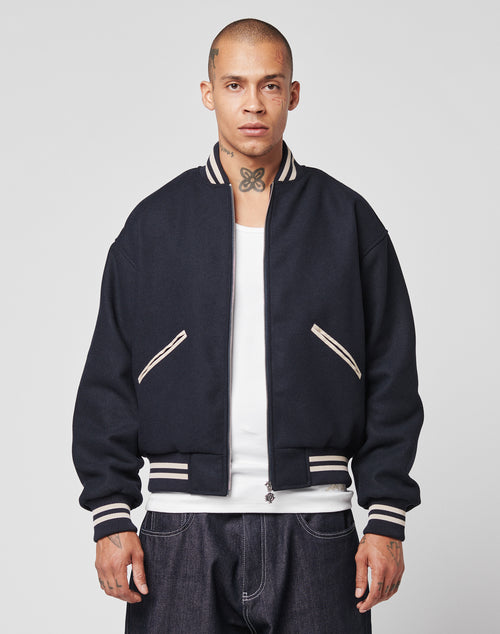 A man with a shaved head and neck tattoo wears the LIVE FAST DIE YOUNG Live Fast College Jacket, a Regular Fit varsity style with DY-Reißverschluss Puller and white trim over a white shirt, facing forward against a plain background.