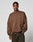 A man stands against a light gray background, wearing the LFDY Wavy Sweater by LIVE FAST DIE YOUNG—an oversized brown sweatshirt with subtle stitching, “LIVE IN PART” on the chest, and paired with dark jeans.