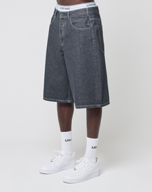 A person in baggy fit LFDY Jorts by LIVE FAST DIE YOUNG with a signature Lederpatch, white crew socks with black text, white sneakers, and white underwear featuring "LIVE FAST" on the waistband stands against a plain light background.