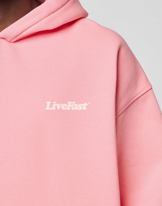 A person wears a light pink Basic 360 Hooded by LIVE FAST DIE YOUNG, featuring white LiveFast text on the chest. The image focuses on the upper section, highlighting topstitching and part of the neck and shoulder.