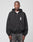 Against a plain light gray background, a person wears the LIVE FAST DIE YOUNG Live Fast Lenox Hooded Zip—an oversize fit black zip-up hoodie with LIVE FAST in white on the chest—paired with faded black jeans. Hands at sides, they have a neutral expression.