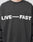 A person wears an Oversize Fit Live – Fast Sweater by LIVE FAST DIE YOUNG, featuring bold white LIVE—FAST text across the chest. The image is cropped to the upper torso and part of the neck. Made from a comfortable Baumwolle blend.