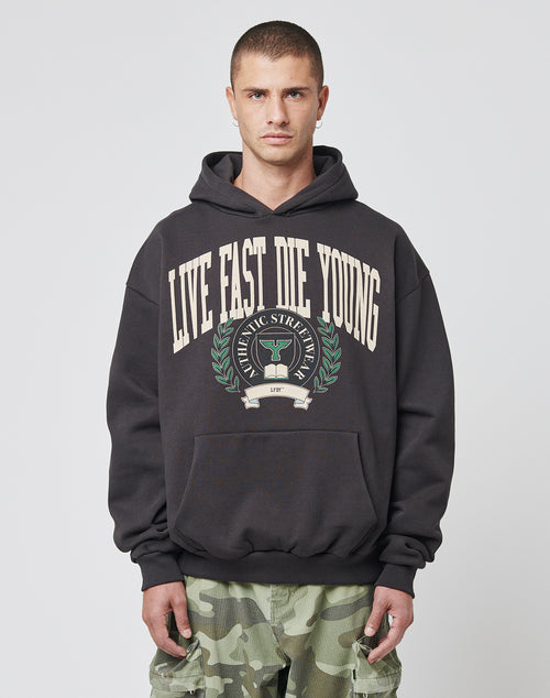 A man with short hair wears the LIVE FAST DIE YOUNG Hooded by LIVE FAST DIE YOUNG, featuring a laurel wreath and trophy graphic, in an oversized fit with subtle topstitching, paired with camo pants against a plain white background.