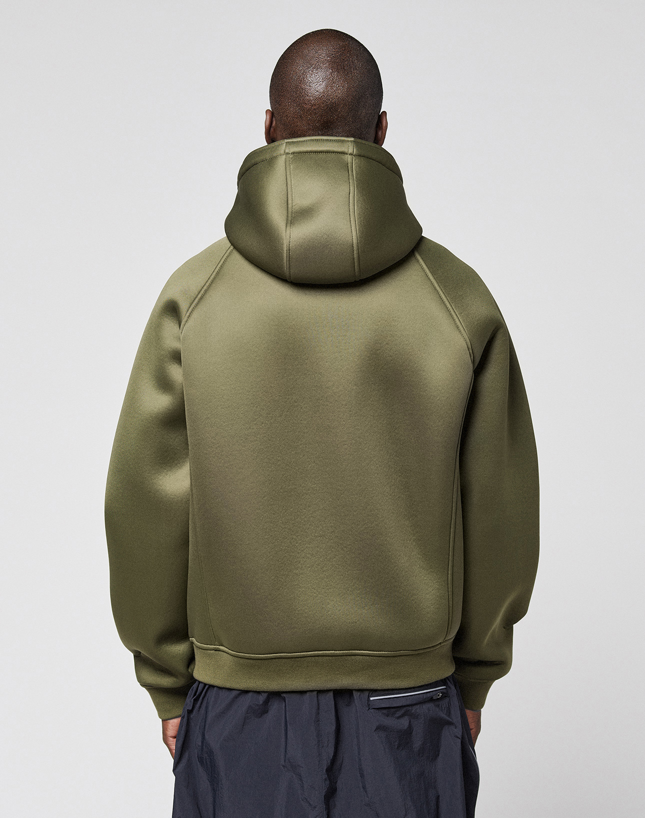 A person with short hair, seen from behind, is wearing a LIVE FAST DIE YOUNG LFDY Scuba Hooded Zip in olive green with zip pockets. The dark, loose Regular Fit pants complete the look against a plain light background.