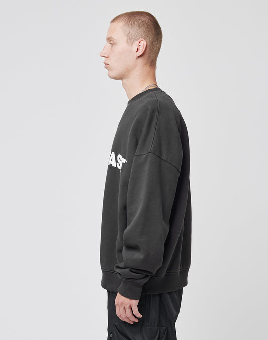 A person with short hair stands in profile against a plain background, wearing the black Live – Fast Sweater by LIVE FAST DIE YOUNG in an oversize fit with white text, made from Baumwolle and polyester, paired with black pants.