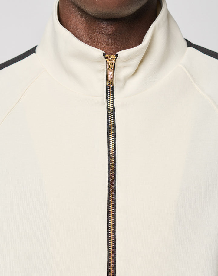 A close-up shows someone wearing the LFDY Striped Track Jacket by LIVE FAST DIE YOUNG, featuring raglan sleeves, a gold zipper, and black shoulder trim. Only the lower half of the face and upper chest are visible.