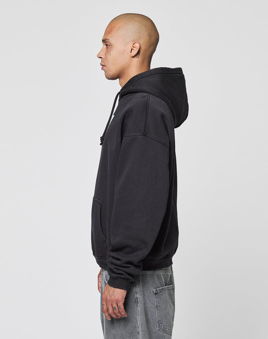A person with a shaved head stands in profile wearing the LIVE FAST DIE YOUNG LFDY Gambling Hooded in black and gray jeans against a plain, light background.