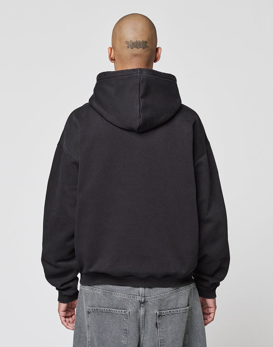 A person with a shaved head and a tattoo on the back of their head is seen from behind, wearing the LIVE FAST DIE YOUNG LFDY Gambling Hooded in an oversize fit with gray jeans, standing against a plain light background.