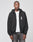 A person wears a LIVE FAST DIE YOUNG Live Fast Lenox Hooded Zip, a black oversize fit zip-up hoodie with front and back print, over a white t-shirt and gray jeans, standing against a plain light gray background with a neutral expression.