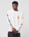 Someone wears the No Rich Parents Longsleeve by LIVE FAST DIE YOUNG—a regular fit, white 100% Baumwolle shirt with orange graphic patches and LIVE FAST in black on the left sleeve—arms crossed against a plain light background.