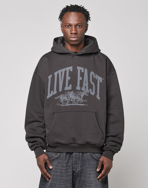 A person wears the LIVE FAST DIE YOUNG Live Fast Stallion Hooded, featuring an oversize fit and bold frontprint, against a plain light background, looking directly at the camera with a neutral expression.