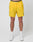 Someone stands against a white background wearing LIVE FAST DIE YOUNG’s bright yellow Live Fast Performance Shorts with a black waistband that reads LIVE FAST, paired with white socks and white sneakers.
