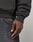 A close-up of a person’s hand resting by their side, wearing the LIVE FAST DIE YOUNG Live Fast Stallion Hooded sweatshirt and faded black jeans with a visible front pocket against a plain, light-colored background.