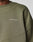 Close-up of a person wearing the LFDY Wavy Sweater by LIVE FAST DIE YOUNG, an olive green oversize fit with LIVE FAST in white on the chest. Made from a soft Baumwolle blend, it has visible stitching and a ribbed neckline.