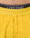 Close-up of a person’s lower torso wearing LIVE FAST DIE YOUNG’s bright yellow Live Fast Performance Shorts with a drawstring, paired with black underwear featuring the words LIVE FAST on the waistband.