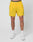 A person stands against a white background wearing LIVE FAST DIE YOUNG Live Fast Performance Shorts in bright yellow with a small left-leg logo and elastic drawstring waist, paired with white socks and sneakers.