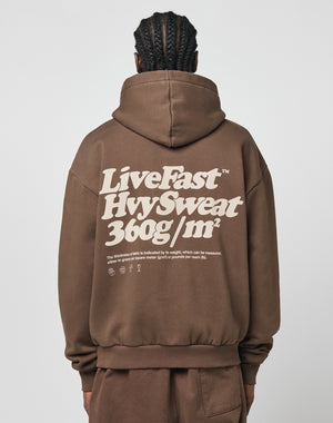 A person with braided hair, seen from behind, wears a brown Basic 360 Hooded hoodie by LIVE FAST DIE YOUNG. Bold white text and smaller print are on the back. The hoodie, made from a cotton-poly blend, is paired with matching brown pants.