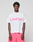 A person wears the LIVE FAST DIE YOUNG Basic OS Livefast Tee in white, featuring a bold pink front print, paired with pink shorts, against a plain light gray background.