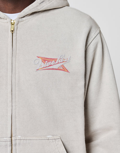 A person wearing a LIVE FAST DIE YOUNG LFDY Corp. Hooded Zip in light beige 100% Baumwolle with a gold zipper, featuring a small colorful graphic and "Time Flies" on the left chest. Only the upper torso is visible.