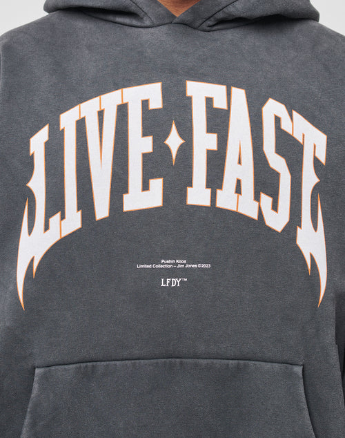 A close-up of the LIVE FAST DIE YOUNG Live Fast Axe Hooded, an oversize dark gray hoodie with bold white and orange LIVE FAST lettering across the chest, soft Baumwolle fabric, and “LFDTM Limited Collection Jan-Jones ©2023” below.