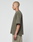 A person with a shaved head and tattoos stands in profile, wearing the LIVE FAST DIE YOUNG Basic +49 Chest Tee in olive green and light-colored shorts against a plain white background.