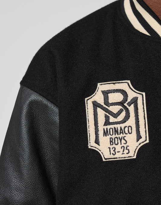 Close-up of the LFDY x Schott NYC Varsity Jacket by LIVE FAST DIE YOUNG, featuring black leather sleeves, a “B1 MONACO BOYS 13-25” chest patch, and classic black-and-white striped collar—signature Schott NYC style.