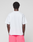 A person faces away from the camera, wearing a LIVE FAST DIE YOUNG Basic OS Livefast Tee in plain white and bright pink shorts with a back pocket, set against a neutral gray background.