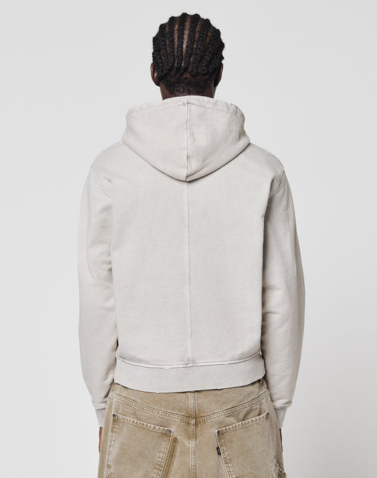 A person with braided hair faces away from the camera, wearing a light beige LFDY Corp. Hooded Zip by LIVE FAST DIE YOUNG and tan pants, standing against a plain white background.