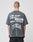 A person with short hair wears the LIVE FAST DIE YOUNG Its Vulgar Tee, a faded black oversized shirt featuring bold front and back prints. The back displays: LIVE FAST™ LUKAS MULLER 2023 370x51 ITS VULGAR in large white text.