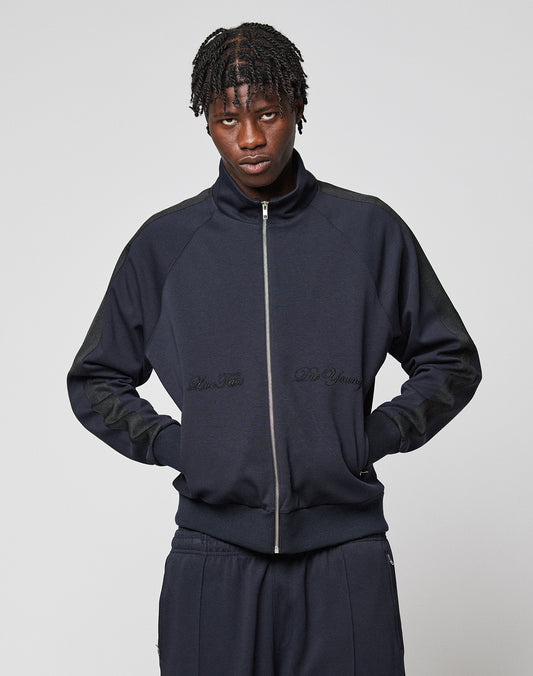 A person with short, twisted hair wears the LFDY Striped Track Jacket by LIVE FAST DIE YOUNG and matching pants, standing with hands in pockets against a plain light gray background.