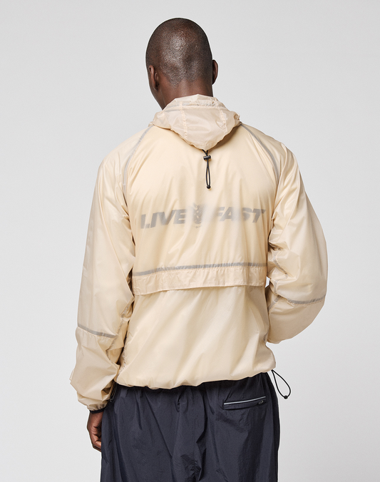 A person wearing the LIVE FAST DIE YOUNG Live Fast Nylon Jacket in light beige, featuring a reflective LIVE FAST print on the back, stands with their back to the camera against a plain background.