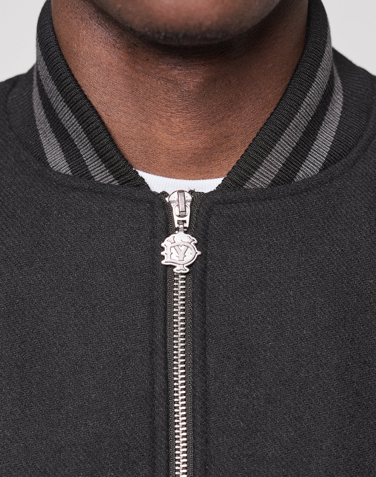 Close-up of a person wearing the LIVE FAST DIE YOUNG Live Fast College Jacket. Features a silver metal zipper with round pull and striped black/gray ribbed collar. Regular Fit offers comfort and style, with the lower face and neck visible.