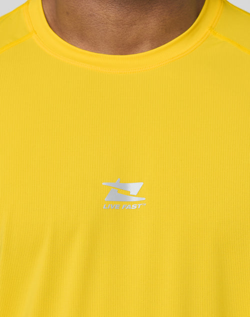 Close-up of a person in the LIVE FAST DIE YOUNG Live Fast Performance Tee, a bright yellow slim fit athletic shirt with a white LIVE FAST logo and reflective chest print. Only the lower face and upper chest are visible.