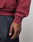 A close-up of a tattooed hand relaxed by the side, wearing the LIVE FAST DIE YOUNG Live Fast Stallion Hooded sweatshirt in maroon and dark blue jeans with white stitching.
