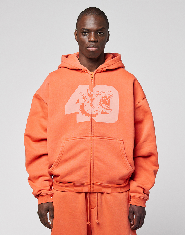 A person wearing the orange LFDY 40 Hooded Zip by LIVE FAST DIE YOUNG, featuring a large number 49 and shark front print, stands against a plain light gray background. | model