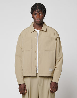 A man with short, textured hair wears the LIVE FAST DIE YOUNG LFDY Padded Shirt over a white top and matching beige pants, standing against a plain light gray background.