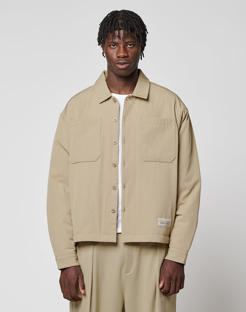 A man with short, textured hair wears the LIVE FAST DIE YOUNG LFDY Padded Shirt over a white top and matching beige pants, standing against a plain light gray background.