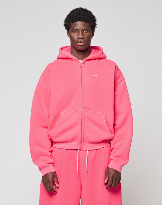A person stands facing forward in an oversized bright pink LIVE FAST DIE YOUNG Basic Hooded Zip with matching sweatpants, set against a plain light gray background.