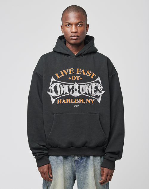 A person faces forward in an oversized black Live Fast Tribal Hooded sweatshirt by LIVE FAST DIE YOUNG, paired with faded blue jeans. The hoodie’s soft cotton-blend fabric offers comfort against a plain light gray background.