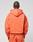 A person faces away from the camera, wearing an oversized orange LFDY 40 Hooded Zip by LIVE FAST DIE YOUNG with the hood down and matching orange pants against a plain light gray background.