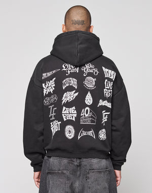 A person faces away from the camera in a black LIVE FAST DIE YOUNG LFDY Logo Hooded Zip, an oversized Baumwolle hoodie with multilogo white graphics and “Live Fast” and “Die Young” phrases on the back, set against a plain gray background.