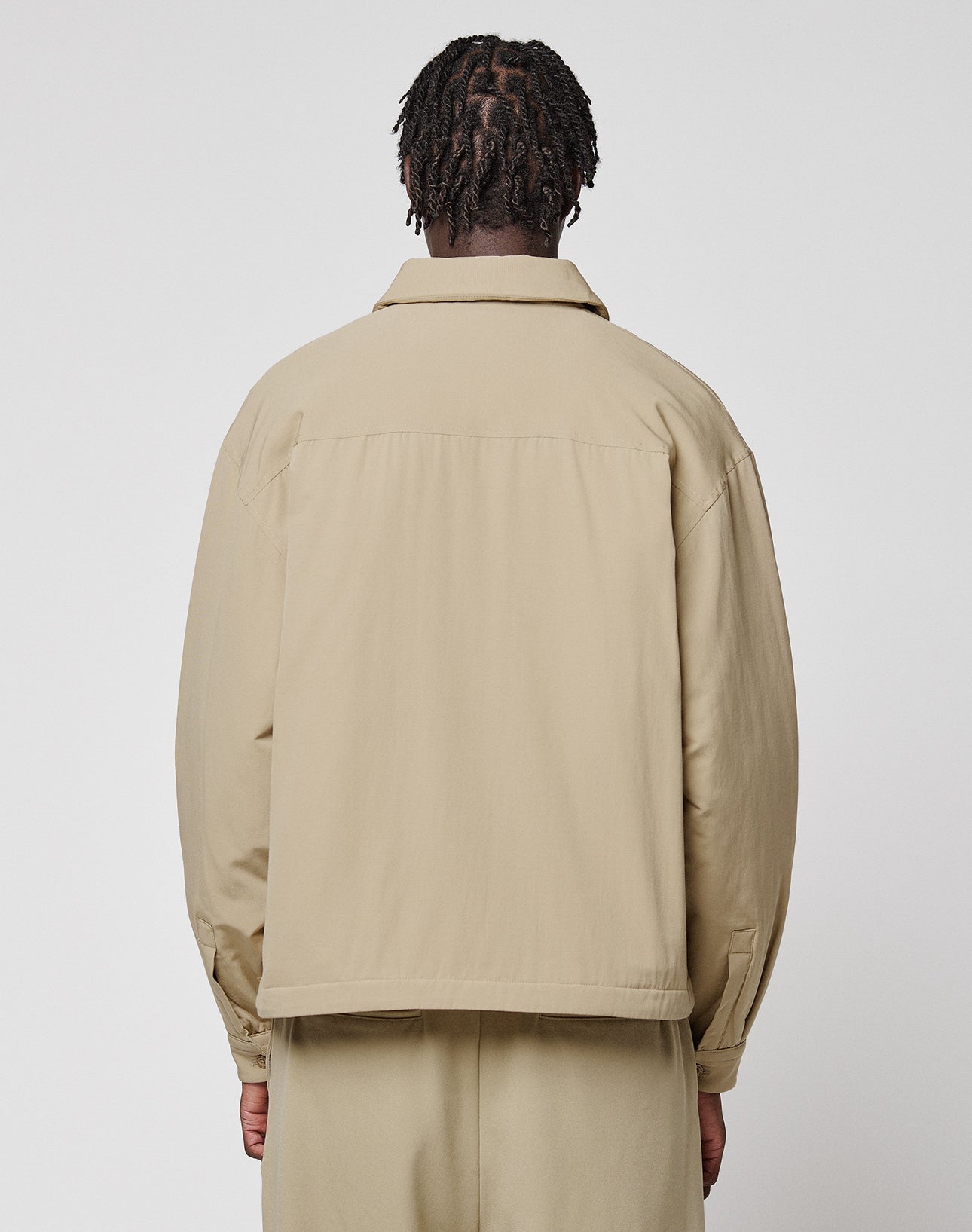 Seen from behind against a plain white background, a person with short, twisted hair wears the beige LFDY Padded Shirt by LIVE FAST DIE YOUNG with matching pants.